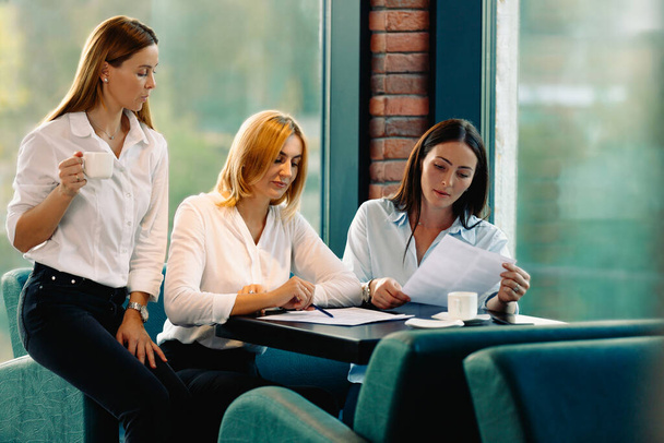 Three female employees working together on a business project in a modern office with a cup of coffee. Teamwork concept. Horizontal, blurred background. High quality photo - Foto, Imagem