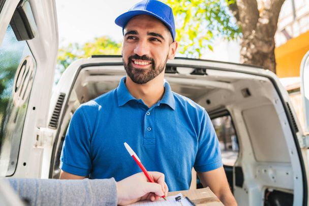 Portrait of a delivery man carrying packages while customer putting signature in clipboard. Delivery and shipping concept. - Фото, изображение