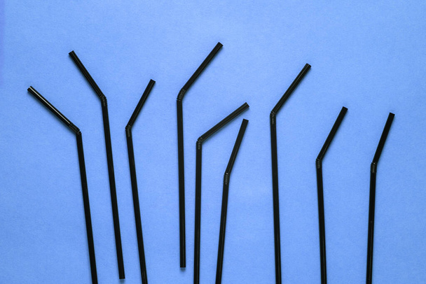 Black cocktail tubes on a blue background. Drinking straws for the party. Top view, flat layout. - Foto, imagen