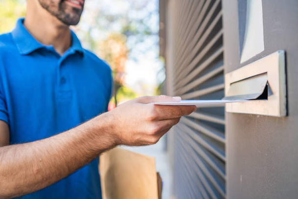 Close-up of a postman putting a letter in a house mailbox. Delivery postal service concept. - Foto, Imagem
