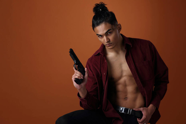 Studio portrait of a young man of Asian appearance with a gun in his hands - Φωτογραφία, εικόνα