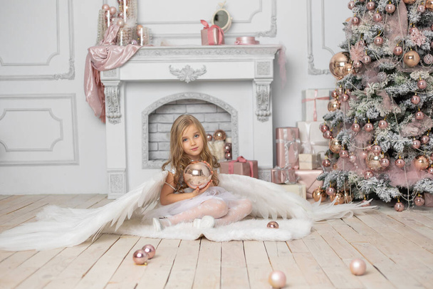 Little cute girl with blond hair with angel wings in the studio next to the Christmas tree and with Christmas balls - Foto, Bild