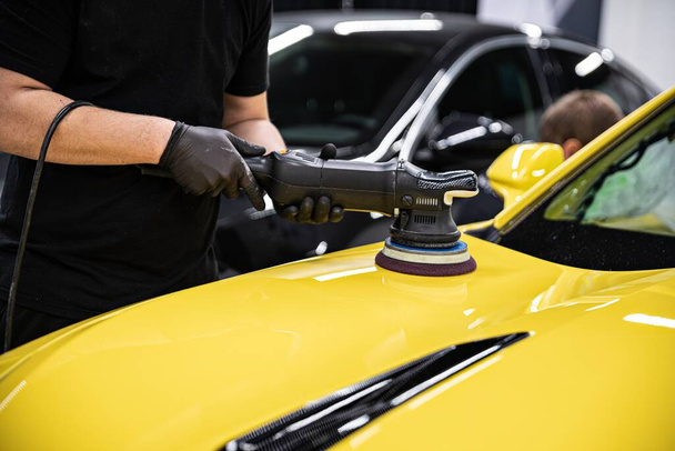 Man car szczegółowo studio pracownik polerowanie żółty lakier samochodowy z polerki elektrycznej - Zdjęcie, obraz
