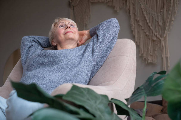 Muhteşem mutlu, yaşlı Avrupalı kadın dinleniyor, iyi haberlerle seviniyor, evinde kanepede oturuyor. - Fotoğraf, Görsel