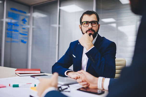 Bearded entrepreneur in optical glasses attentively listening business proposal from cropped partner during meeting in office interior, corporate director discussing productive strategy with employee - Φωτογραφία, εικόνα