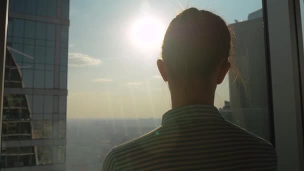 Töprengő nő nézi városkép ablakon keresztül felhőkarcoló - visszapillantás - Felvétel, videó