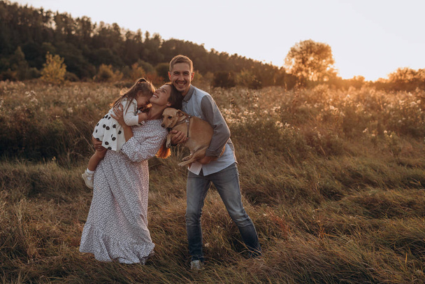 Щаслива сім'я батько і мати і дочка з собакою, що ходить на природі на заході сонця
 - Фото, зображення