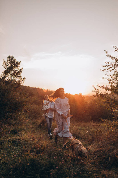 Glücklicher Familienvater und Mutter und Tochter mit Hund spazieren bei Sonnenuntergang in der Natur - Foto, Bild