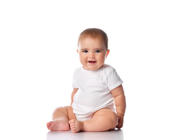 Little baby girl in white bodysuit sitting on the floor isolated on white. - Фото, изображение