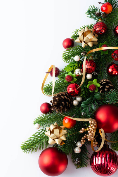 Fragment eines Weihnachtsbaums mit Dekor in rot-goldenen Tönen auf weißem Hintergrund mit Platz zum Schreiben von Text. Weihnachtskarte. - Foto, Bild