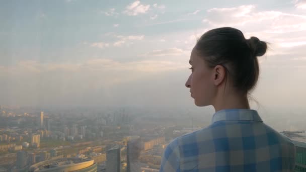 Vista posterior de la mujer mirando el paisaje urbano a través de la ventana del rascacielos - Metraje, vídeo