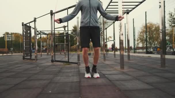 Sportlicher Mann springt mit Springseil-Workout im Freien. Der Mensch benutzt Springseil. Cardio-Workout im Fitnessstudio. Sportanfänger üben grundlegende Sprünge mit Springseil. Übungen für eine schnelle Gewichtsabnahme - Filmmaterial, Video