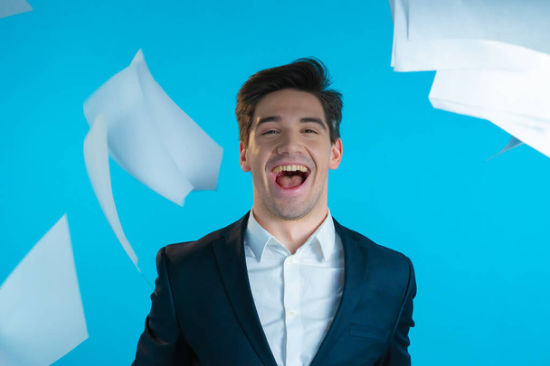 Businessman throwing papers documents into air and celebrates success on blue background. Freedom, successful completion of project concept. - Foto, Bild