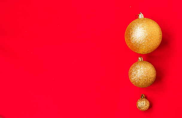 Three golden Christmas balls of different sizes are displayed in a row as a border on a red background. New Year mood mok up. Copy space - Φωτογραφία, εικόνα