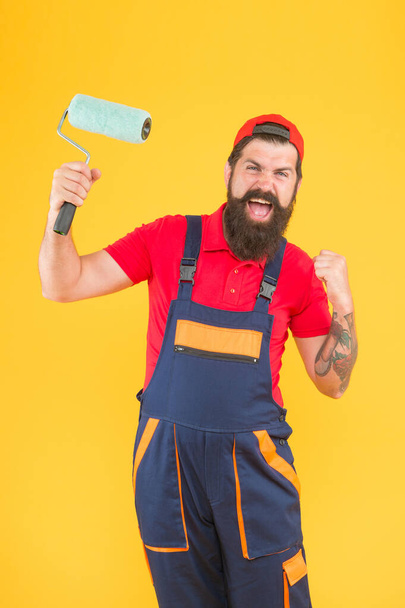 happy brutal man in boilersuit uniform. mature hipster use paint roller tool for painting. repairman or builder working. creative idea. foreman going to make wall facing. exploring tools - Foto, Imagem