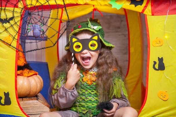 Маленькая милая девочка, одетая как лесная фея, сидит в детской палатке, украшенной на Хэллоуин летучими мышами и призраками, паутина с пауком, оранжевые тыквы. - Фото, изображение