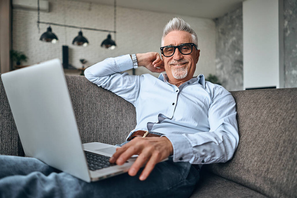 Smiling adult man resting at home while working with laptop. Home and lifestyle concept. Self Isolation - Foto, immagini