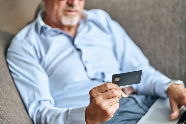 Cropped photo of bearded mature man with laptop and credit card staying at home while shopping online. Lifestyle concept - Фото, зображення