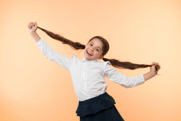 Happy girl show long brunette hair on yellow background. Little child smile with new hairstyle. Hairdresser salon services. Proud of her beautiful hair. Beauty salon. Stylish and cute - Photo, image