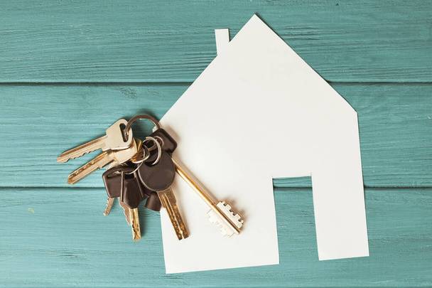 Haussymbolpapier mit silbernen Schlüsseln auf türkisfarbenem Holzhintergrund. Neues Hauskonzept. Kauf einer neuen Wohnung. Pacht und Miete - Foto, Bild