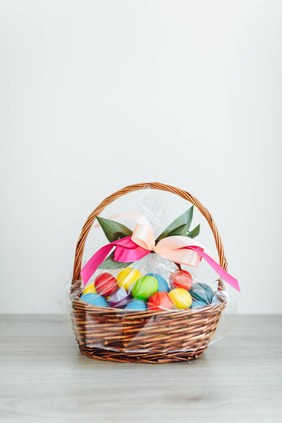 Easter color eggs in festive gift basket, light gray wooden background with copy-space - Photo, image
