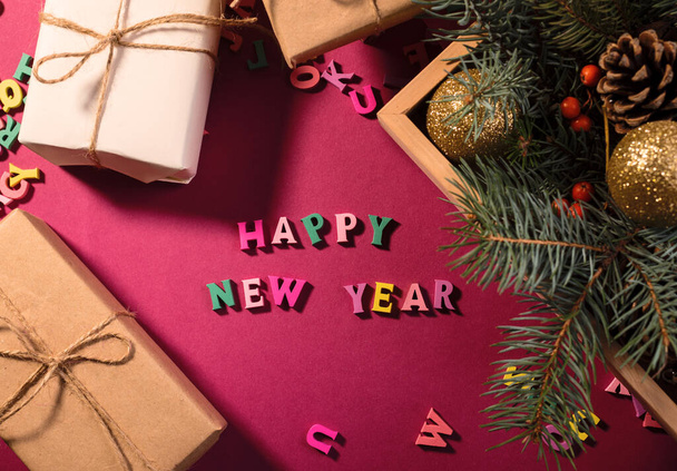 Happy New Year kaart of banner met begroetingswoorden gemaakt van houten letters, geschenkdozen op een paarse achtergrond versierd met feestelijke dennenbomen takken. - Foto, afbeelding