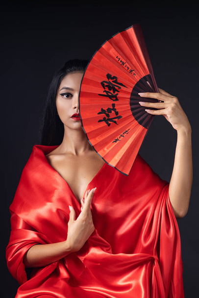 Geyşa gibi giyinmiş, kırmızı kimonolu ve yelpazeli güzel bir kız. - Fotoğraf, Görsel
