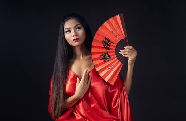 on a black background Chinese girl with red lips and in a red traditional Chinese gown - 写真・画像