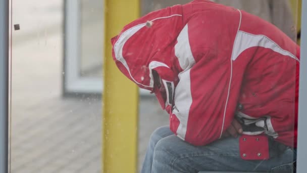 Un hombre irreconocible con una chaqueta roja se sienta en una parada de transporte público. Sin cara. - Metraje, vídeo