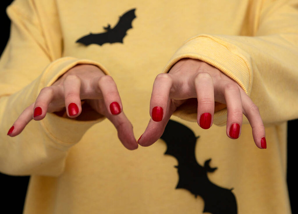 um homem expôs garras com manicure vermelho em suéter amarelo com morcegos pretos - Foto, Imagem