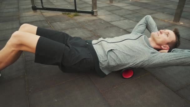Man doing exercises on foam roller outdoor. Male stretching his back over vibrating foam roller for physical therapy. Health, injury concept. Massager for relaxation, stretching muscles and back pain - Footage, Video