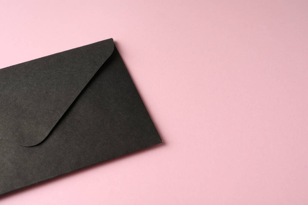 Black paper envelope on pink background, closeup. Space for text - 写真・画像