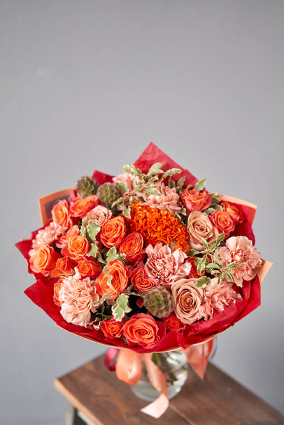 Kırmızı ve turuncu çiçekler. Ahşap masadaki cam vazoda karışık çiçeklerden oluşan sonbahar buketi. Çiçekçi dükkanındaki çiçekçinin işi. Taze kesilmiş çiçek.. - Fotoğraf, Görsel