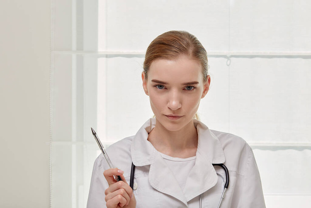 A female doctor in a medical gown looks at the camera with a serious expression. - Foto, immagini