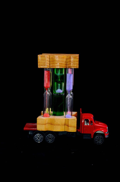 Time Transportation Concept Zandloper Kijk op een rode speelgoedauto over zwarte achtergrond - Foto, afbeelding