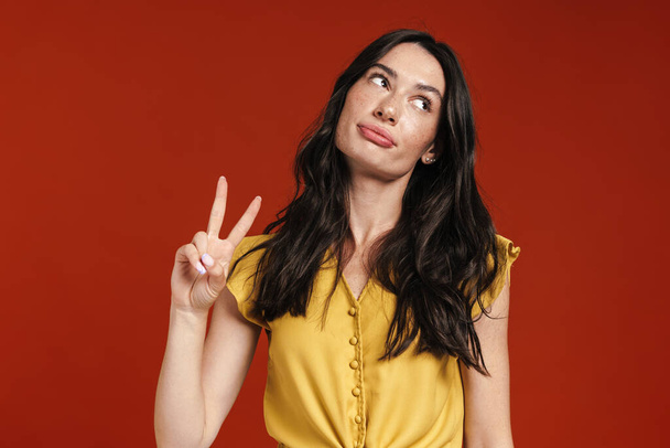 Image of young displeased woman showing peace sign and looking aside isolated over red background - Foto, Imagem