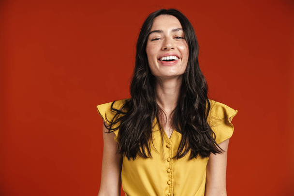 Image of young happy woman smiling and looking at camera isolated over red background - Фото, изображение