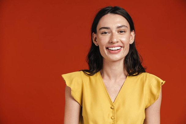 Image of young happy woman smiling and looking at camera isolated over red background - Photo, image