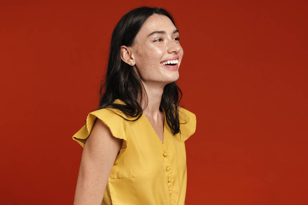 Image of young happy woman smiling and looking aside isolated over red background - Foto, Imagen