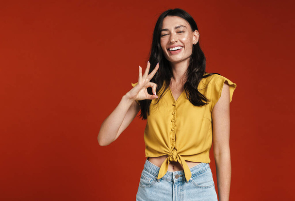 Image of young happy woman smiling and making ok gesture isolated over red background - Fotó, kép