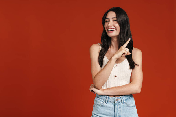 Image of young happy woman smiling and pointing finger aside isolated over red background - Foto, Imagem