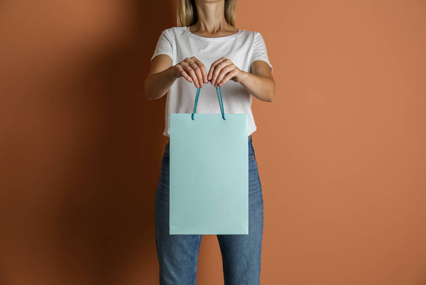 Woman with paper shopping bag on light brown background, closeup - Φωτογραφία, εικόνα