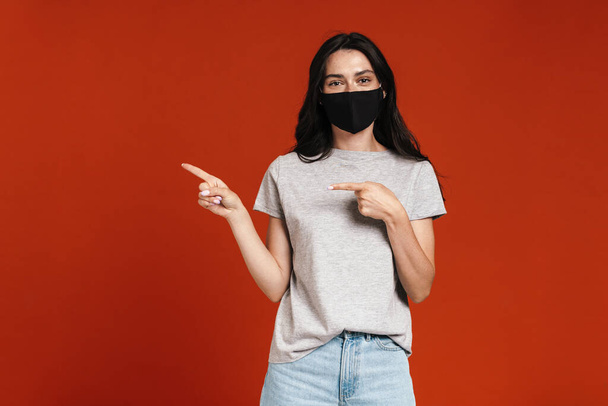 Image of young pleased woman in face mask pointing fingers aside isolated over red background - Foto, afbeelding