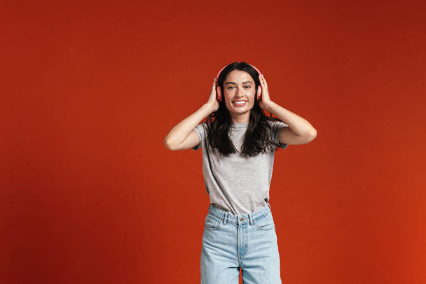 Image of young happy woman smiling and using headphones isolated over red background - Fotó, kép