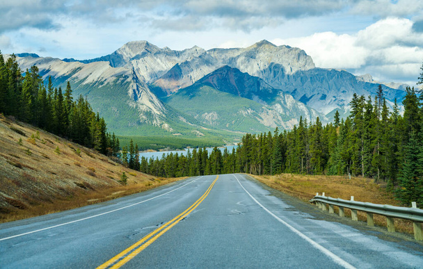 Camino rural en el bosque con montañas en el fondo. Alberta Highway 11 (David Thompson Hwy) a lo largo de la orilla del lago Abraham. Parque Nacional Jasper, Canadá. - Foto, Imagen