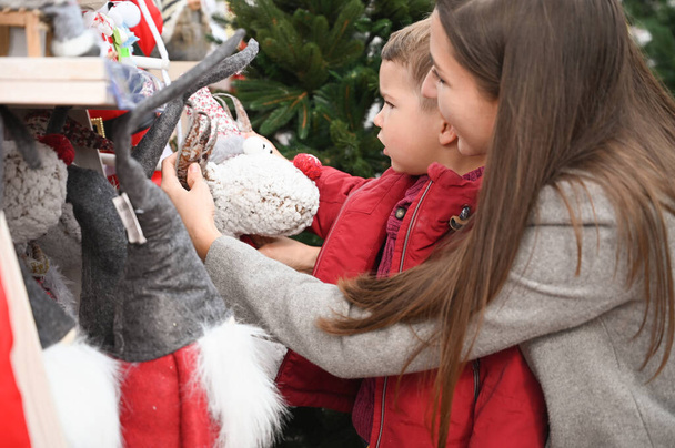 Äiti ja lapsi valitsevat joulun lelut myymälän hyllyllä - Valokuva, kuva