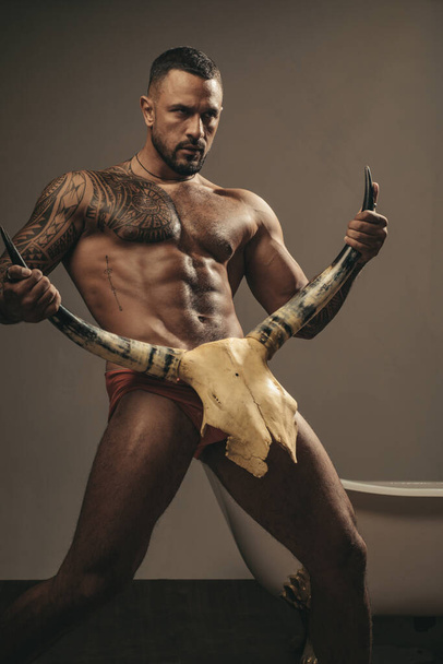 Strong sexy nude man with bull skull on grey background. - Foto, imagen