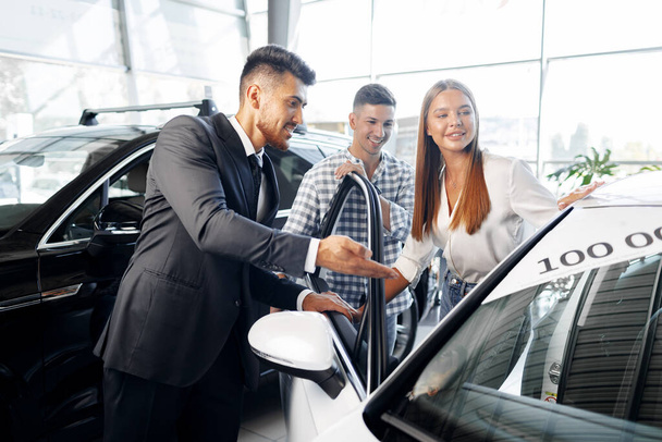 Young couple choosing a car at the dealership with manager helping - Foto, immagini