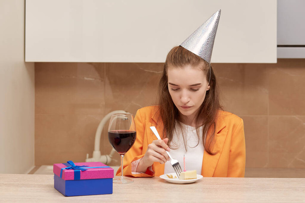 Young woman eating birthday cake. On the head of a festive cap of silver color. - Photo, Image