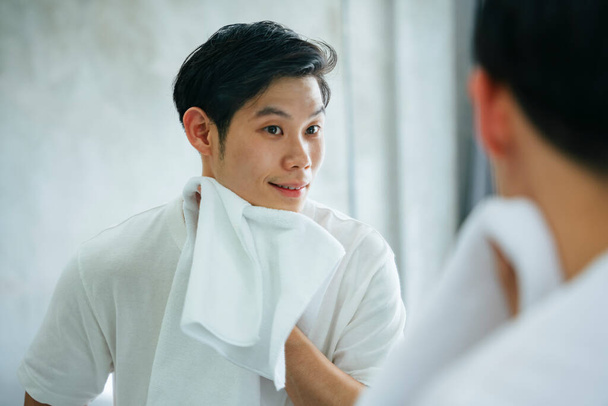Asiatique jeune homme nettoyage visage avec serviette dans la salle de bain. - Photo, image